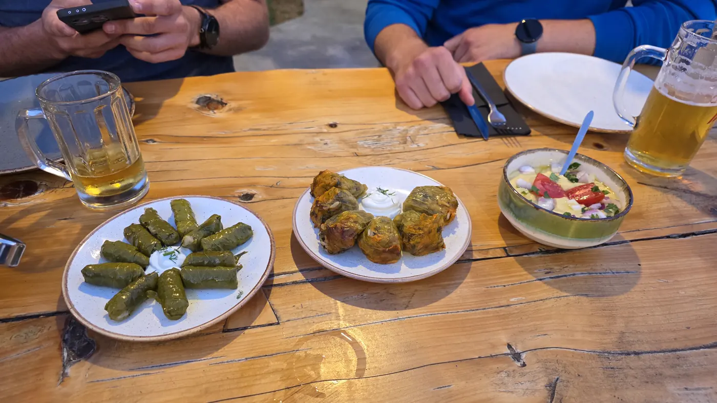Gefüllte Weinblätter, gefüllte Zucchiniblüten und ein Dip auf einem Holztisch, daneben Bier
