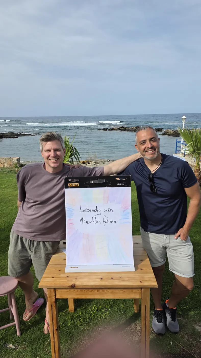 Andreas und Johannes am Meer neben einem Flipchart mit „Lebendig sein. Menschlich führen.“