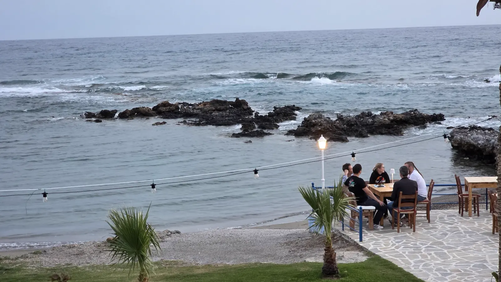 Die Gruppe beim Abendessen auf einer Terrasse direkt am Meer, in der Dämmerung mit Laterne und Lichterkette
