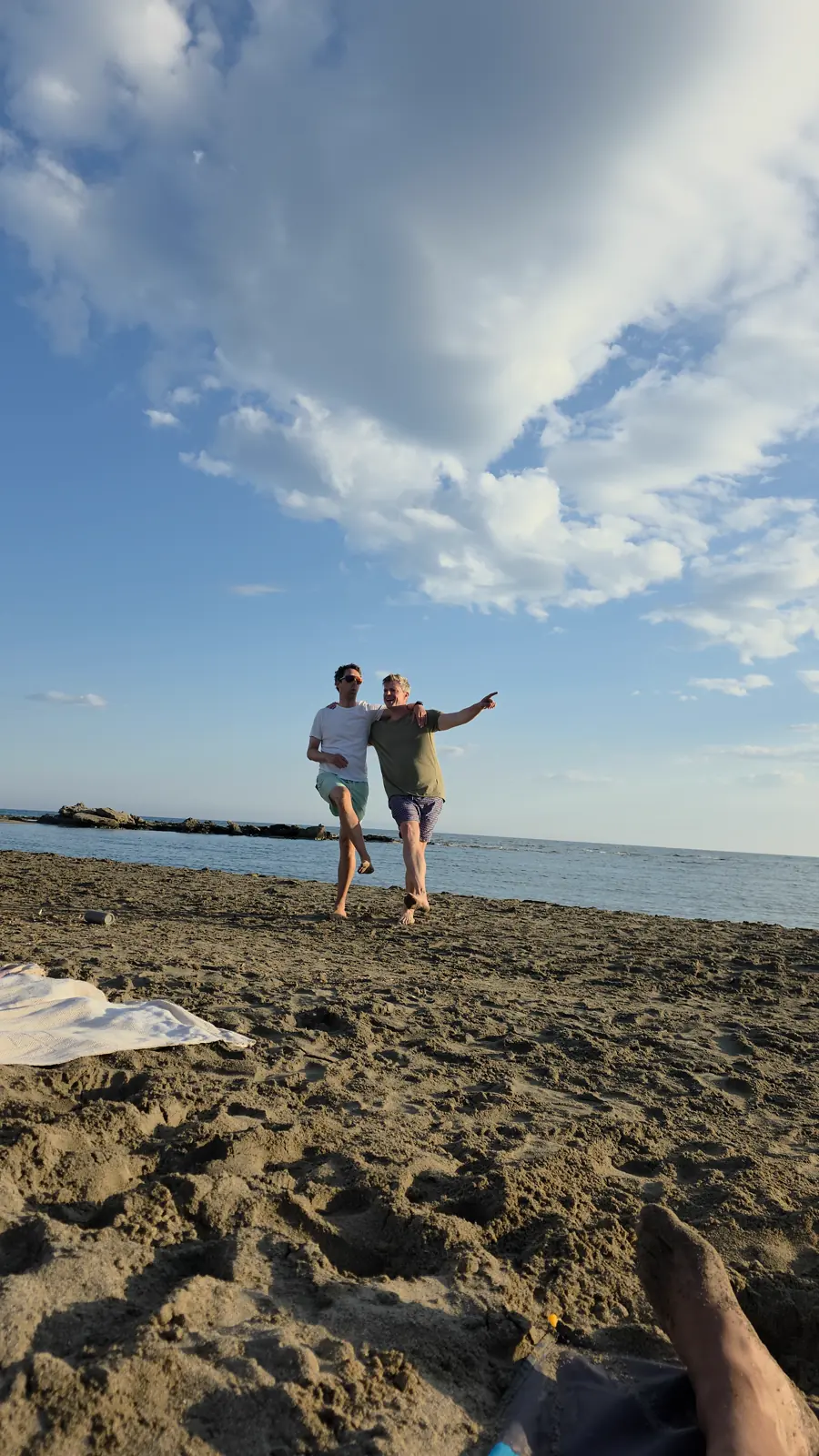 Zwei Teilnehmer ziehen lachend Arm in Arm über den Strand, dahinter Meer und Wolkenhimmel